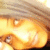 A pixelated close-up of a person's face with light brown hair, showing eyes and part of the nose against a warm-toned background.