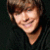 Pixelated close-up of a smiling person with brown hair against dark background, static image.