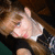 Pixelated image of a person with light brown hair wearing dark clothing, making a hand gesture near their face.