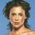 Pixelated portrait of a person with dark curly hair against a solid blue background, showing a neutral expression and bare shoulders.