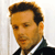 Static pixelated image of a man's face and upper torso in formal attire against a light background.