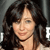 A pixelated close-up of a person with dark wavy hair, light skin, and a neutral expression against a dark background with partial white text.