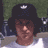 Static pixelated icon of a person with dark hair and brown skin wearing a white shirt, set against a green background with blurred elements.
