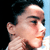 Pixelated close-up of a person's face in profile, showing dark hair, light skin, and a neutral expression against a black and light blue background.
