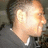 Pixelated static image of a person's face with light skin tone, dark hair, and visible ear against blurred background.