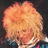 Pixelated close-up of a person with light brown curly hair against dark background, wearing blue and pink clothing.