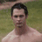 A shirtless man with dark hair stands against a grassy background; the right side shows a green screen with pink pixelated text.