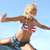 Pixelated image of a person with light hair in a dynamic pose, wearing a red and white striped bikini top with blue accents, dark shorts, and a small red and white symbol on the chest.