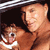 A pixelated image shows a person holding a small brown hamster with white markings on its face and chest, both facing forward against a dark background.