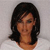 Pixelated portrait of a person with dark shoulder-length hair against a light gray background, wearing a white top.