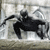 Black silhouette of a figure in dynamic pose with extended limbs against light gray background, rendered in low-resolution pixel art style.