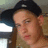 Pixelated close-up of a person wearing a black cap with a white logo, brown hair, and a light-colored top against a blurred background.