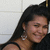A woman with long dark hair and silver earrings smiles, wearing a black sleeveless top against a white tiled background.