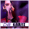 Pixelated image of a person with dark hair holding a microphone, wearing a red outfit with a white collar, against a purple background with light speckles.