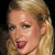 Pixelated close-up of a person with light brown hair tied back, wearing red lipstick, against a dark background.