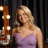 Static pixelated image of a woman in a light purple dress with blonde hair, standing next to an illuminated sign against dark vertical stripes.