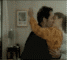 A couple in formal attire embraces and kisses , with the woman wearing an orange dress and the man a dark suit