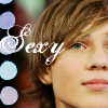 A close-up of a person's face with brown hair, overlaid with the word 'Sexy' in white cursive script and blue-purple circular bokeh lights in the background.