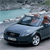 Pixelated static image of a light blue convertible car with dark blue accents, positioned on a road under a cloudy sky.