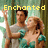 Two people in a forest pose with raised arms, wearing green and gray clothing under yellow text reading 'Enchanted me do come'.
