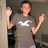 Pixelated image of a person in gray shirt with white logo, arms raised against muted background.