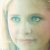 Pixelated close-up of a person's face with light skin, blue eyes, and visible hair strands on the left side.