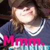 A person with light brown hair wearing a dark blue shirt with white trim, smiling with eyes closed and pink text reading "Mmm." overlaid at the bottom.