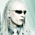 Static pixelated image of a person with long light-colored hair wearing dark sunglasses and a dark tie against a pale background.