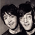Two pixelated human faces with dark hair and light skin tones appear side-by-side against a gray background, both smiling with closed mouths.