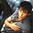 A pixelated image of a person lying down with arms crossed, wearing dark clothing and light-colored sleeves, against a blurred background.