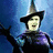 A pixelated witch figure in a purple robe and pointed hat stands against a blue background, with green text reading "I'm through with playing by the rules of someone else's game" and "Defy Gravity.".