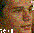 Pixelated static image of a person's face with visible text at the bottom, rendered in low-resolution mosaic style on a dark background.