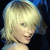 Pixelated close-up of a person with short blonde hair, light skin, and a faint smile against a dark background with blue accents.