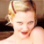 Pixelated close-up of a person with light brown hair styled in a side part, wearing red lipstick and a dark strap over one shoulder.