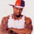 Static pixelated image of a person wearing a red and blue cap, white tank top, and dark shorts with visible tattoos on arms.