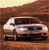 Pixelated image of a light-colored sedan with dark windows and black wheels, positioned on a brown textured surface under a pale sky.