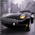 Pixelated image of a dark vehicle with illuminated headlights against a gray urban backdrop with tall buildings.