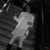 Pixelated grayscale image of a stylized figure with outstretched arms and legs against a dark background with faint horizontal lines.