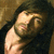 Pixelated image of a person with long dark hair covering their face, wearing a dark top against a brownish background.