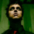 Pixelated static image of a person's face and upper torso against green background with dark clothing and red accent.