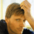 A pixelated close-up of a person with light brown hair, wearing a dark shirt, holding a white object near their face.