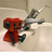 Red cartoon character with black accents sits in a light-colored sink holding a silver faucet, smiling.