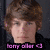 Pixelated image of a person with brown curly hair and light skin, wearing a dark top, with purple text at the bottom.
