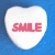 A heart-shaped candy icon with red text reading SMILE on a blue background, shown in two nearly identical frames of an animation.