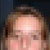 Pixelated close-up of a person's face with light skin tone and brown hair against a dark background.