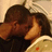 Two figures in close physical contact with dark hair and brown skin tones, one figure's hand near the other's face against a light background.