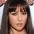 A pixelated close-up of a person with long brown hair and bangs, wearing a dark choker necklace, with red floral shapes in the top corners.