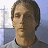 Pixelated portrait of a person with short brown hair wearing a light-colored shirt against a blurred background with blue and white tones.