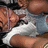 A pixelated static image shows a person with light brown hair wearing a white shirt and dark jacket, holding an object near their face.