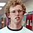A pixelated image of a person with curly light brown hair wearing a white shirt with black collar, set against red background with text overlays.